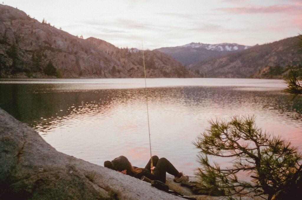 Girl fishing from rock on mountain lake.