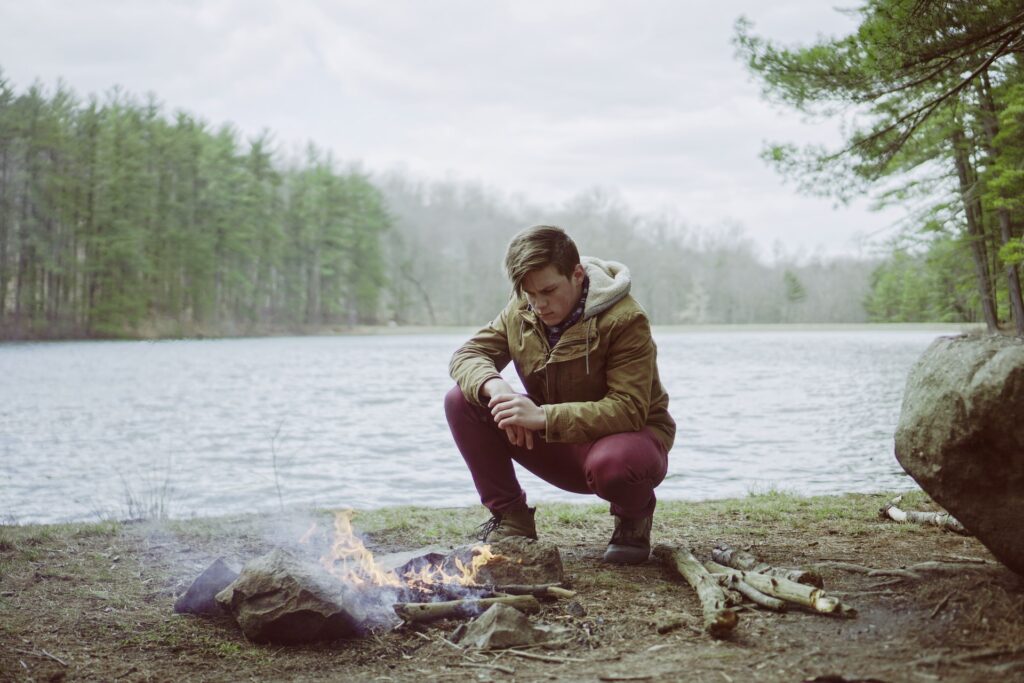 Man making fire on lake beach in forest.
