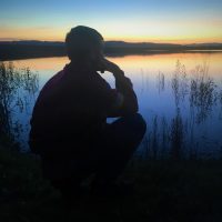 Man kneeling by lake.